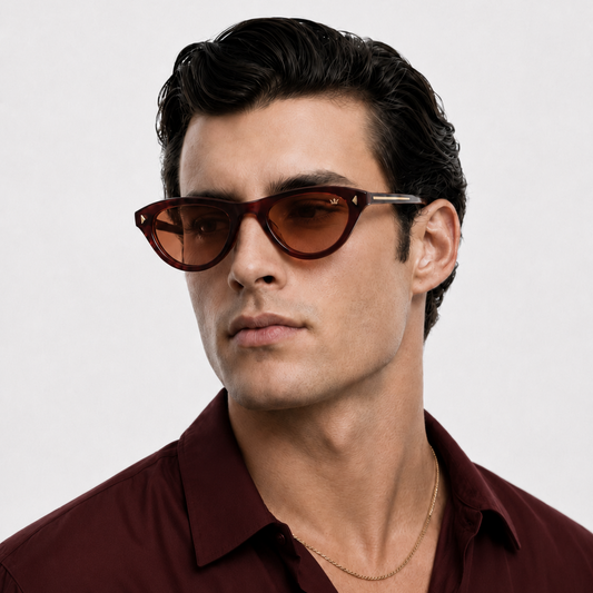 A man wearing cat-eye sunglasses with dark brown frames and tinted lenses, paired with a burgundy button-down shirt against a light gray background.